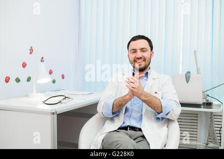 Medico seduto rilassato nella sua sedia in ufficio e sorridente Foto Stock