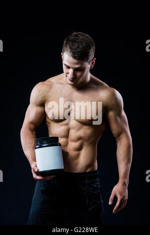 Allestitore tenendo un nero vaso in plastica vuoto etichetta bianca la proteina del siero di latte e che puntano ad esso con la sua mano isolato su sfondo scuro Foto Stock