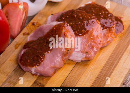 Fette di pezzi di carne cruda per barbecue con ortaggi freschi pomodori, lattuga su una superficie di legno Foto Stock