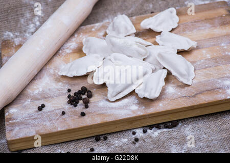 Realizzazione di gnocchi fatti in casa la pasticceria tortellini o ravioli. Modello per la pasta fatta in casa ripiena di carne. Preparazione di pasti organici su una scrivania in legno. Foto Stock