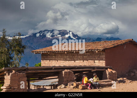 Due bambini seduti al di fuori di un adobe house nel villaggio andino di Misminay, Perù Foto Stock