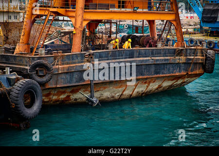 Due lavoratori su una chiatta enorme ispezionare le acque intorno al lavoro che stanno facendo nel porto di Victoria e di Hong Kong. Foto Stock