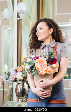 Attraente sorridente giovane donna fioraio permanente e la holding Vaso con fiori in negozio Foto Stock