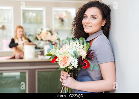 Ritratto di felice piuttosto giovane donna fioraio con bouquet di fiori in piedi nel negozio di fiori Foto Stock