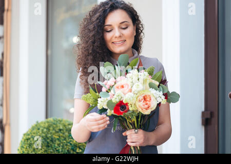 Sorridente carino donna giovane fioraio con bouquet di fiori in piedi nella parte anteriore del negozio Foto Stock