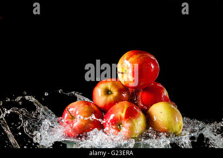 Poche le mele rosse che giace sul lato di argento e battenti di acqua su uno sfondo nero Foto Stock