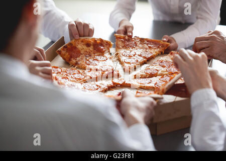 Il team Aziende di mangiare la pizza in ufficio seduti attorno al tavolo Foto Stock