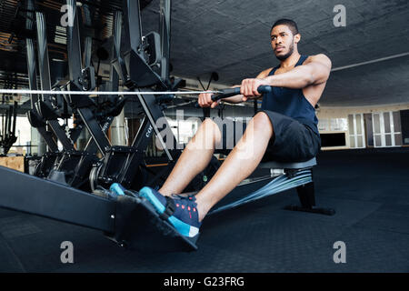 Montare muscolare uomo con vogatore in palestra Foto Stock