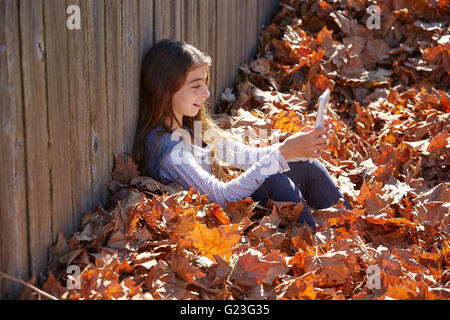 Tween kid girl riproduzione di tablet pc in foglie di autunno Foto Stock