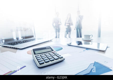 I dati finanziari documenti, calcolatrice e laptop, tre uomini d'affari in piedi sullo sfondo Foto Stock