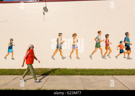 Una donna cammina davanti a un muro dipinto murale di guide a via Baracca negozio di sport nel quartiere alla moda di Colonialtown North Orlando, in Florida. Foto Stock