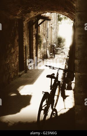 Antico passaggio di ciottoli con case di pietra e di biciclette supportato su facciate retroilluminato Foto Stock