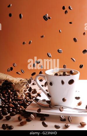 I chicchi di caffè che cade su di un tavolo di legno con tazza di caffè e sacco Foto Stock