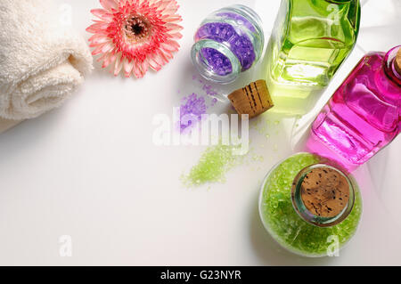 Oli e sali da bagno bianco sul tavolo di vetro. Decorata con fiori e asciugamano. Composizione orizzontale. Vista superiore Foto Stock