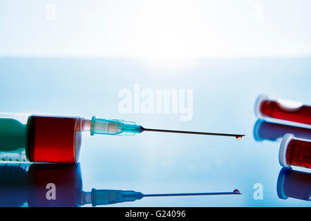 Siringa e fiale con campionamento del sangue su blue tavolo di vetro e lo sfondo. Composizione orizzontale. Vista frontale. Foto Stock