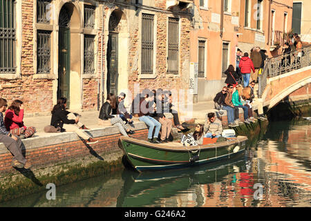 Giovani godendo una giornata di sole in un canale di Venezia in primavera Foto Stock