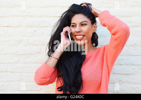 Giovane bella donna latina parlando al telefono. Donna che utilizza un telefono cellulare di indossare un abbigliamento informale. Foto Stock