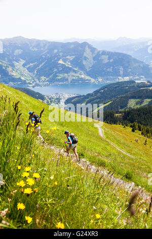 Due persone escursionismo fino alla cima della montagna di Schmitten o Schmittenhohe con il lago di Zell in background, Zell am See, Austria, Europa Foto Stock