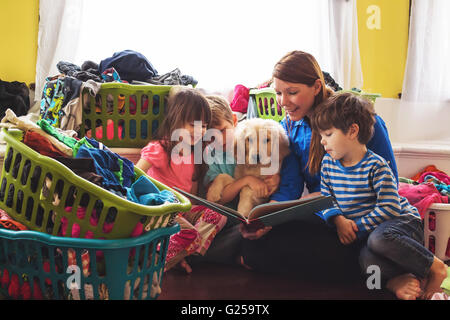 Sorridente lettura madre di tre bambini e golden retriever cucciolo di cane circondato da cesti per la biancheria Foto Stock