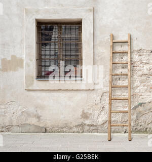 Abbandonato incrinato un muro di mattoni con una finestra e la scaletta di legno Foto Stock