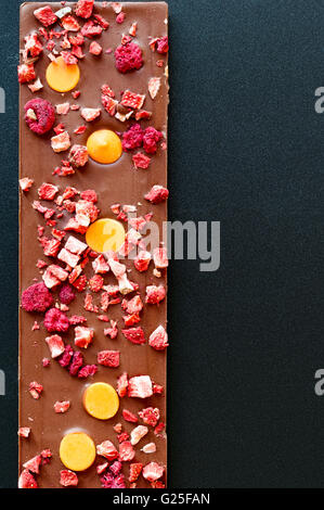 Vista dall'alto di un'arancia, fragola e lampone latte tavoletta di cioccolato su un nero, sfondo sgranate. Foto Stock