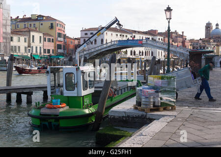 Un uomo cammina via con un carrello a mano dopo che è stato svuotato in una barca di rifiuti sul Canal Grande Foto Stock