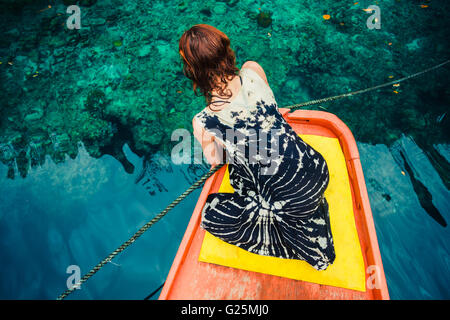 Una giovane donna è seduta su una barca e sta esaminando le chiare acque blu Foto Stock