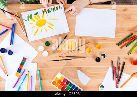 Vista dall'alto le mani di madre e figlio di verniciatura con vernici ad acquerello insieme sul tavolo Foto Stock