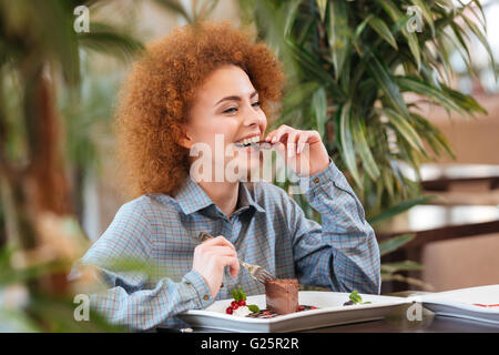 Felice bella redhead giovane donna seduta al cafe e mangiare i dessert al cioccolato Foto Stock