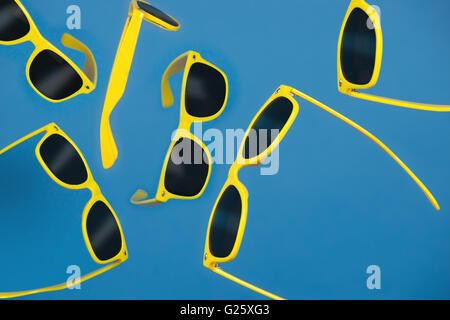 Di plastica gialla viandante sfumature di stile con lenti nere sparato contro un blu di sfondo per studio. Foto Stock