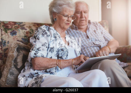 Ritratto di vecchia donna seduta con il marito e con tavoletta digitale. Coppia senior seduti sul divano di casa con un tocco scre Foto Stock