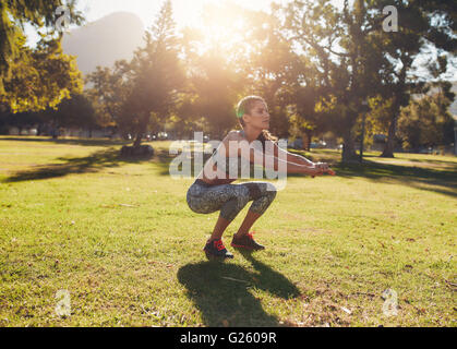 Lunghezza piena ripresa esterna di montare la giovane donna che esercitano nel parco. Ella facendo squatting in una mattina di sole. Foto Stock