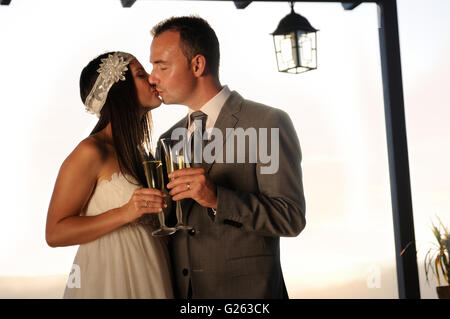 Lo sposo e la sposa baciare e tostatura su un terrazzo a mezza lunghezza Foto Stock