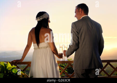 Lo sposo e la sposa la tostatura con champagne su una terrazza a sorridere il contatto visivo vista posteriore Foto Stock