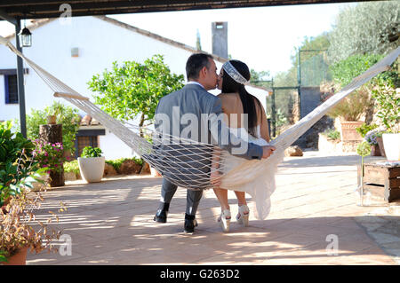 Lo sposo sposa kissing seduta in una amaca corda sulla terrazza di una casa di campagna Foto Stock