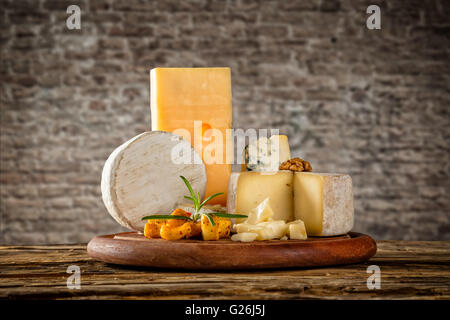 Vari tipi di formaggio collocato sul tavolo di legno, copyspace per testo. muro di mattoni su sfondo Foto Stock