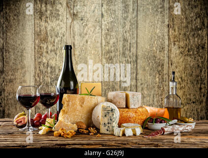 Vari tipi di formaggio, bicchieri e una bottiglia di vino rosso collocato sul tavolo di legno, copyspace per il testo. Tavole di legno su sfondo Foto Stock