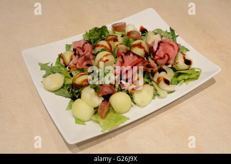 Piastra quadrata con insalata leafes, melone, uva, prosciutto e aceto balsamico Foto Stock