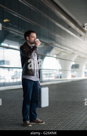 Giovane uomo bello con tazza di caffè e la valigia in aeroporto Foto Stock