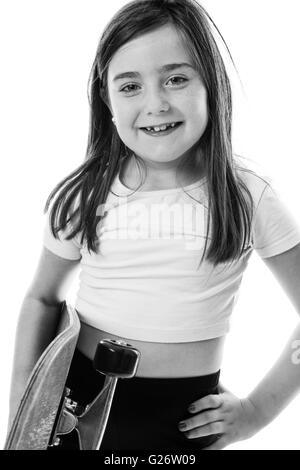 Cheeky giovane ragazza con il suo skateboard con una mano e con il suo altro sulla sua anca. Foto Stock