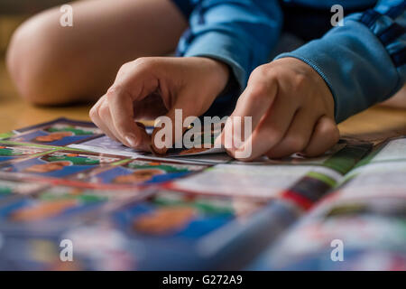 Un bambino di 8 anni del ragazzo è incollare il calcio carte commercio nella sua sticker collection scrapbook. Foto Stock