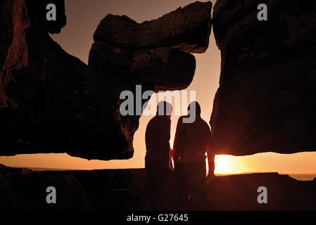 Portogallo: Silhouette di due persone a guardare il tramonto panoramico con curiosa formazione rocciosa a Capo Carvoeiro Foto Stock