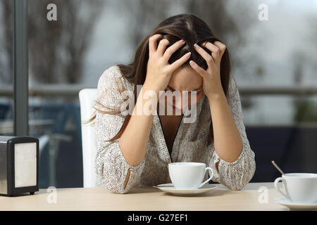 Triste e depresso donna da sola in un solitario bar dopo una pausa con una piovosa giornata invernale all'aperto in background Foto Stock