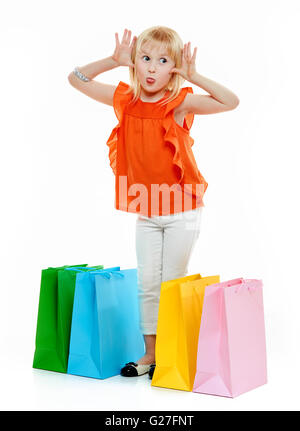 Colorati negozi vibes. A piena lunghezza Ritratto di giovane bionda ragazza in maglietta arancione in piedi vicino a sacchetti colorati e agire la scimmia Foto Stock