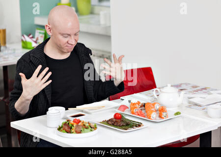 Giovane uomo seduto al sushi bar, sorridente Foto Stock