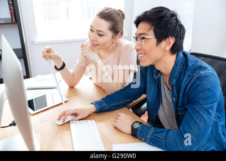 Sorridente giovane uomo e donna che lavorano con il computer in ufficio insieme Foto Stock