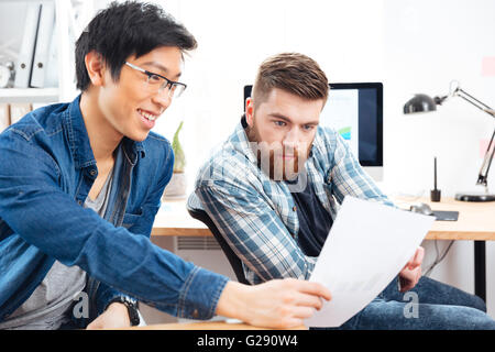 Due bello pensieroso giovani uomini seduti e lavorare con documenti di office Foto Stock