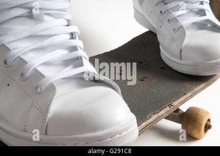 Uomo in bianco pulito formatori fare trucchi su un vecchio skateboard Foto Stock