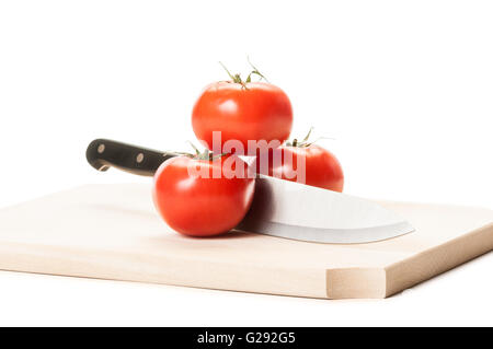 Grande coltello in acciaio tra tre pomodori rossi sulla tavola di legno con sfondo bianco Foto Stock