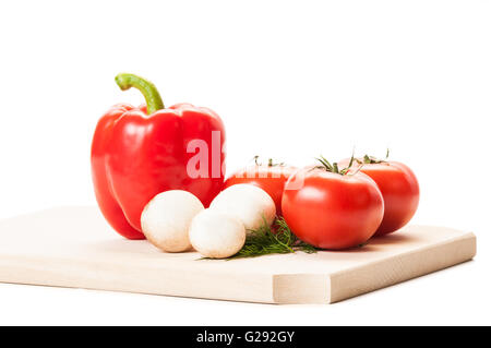 Alcuni funghi champignon, tre pomodori, uno rosso pepe e alcune aneto sul piatto di legno e sfondo bianco Foto Stock